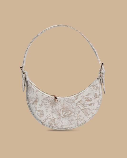 The Flora block-print shoulder bag — three-quarter view of the ivory floral crescent silhouette