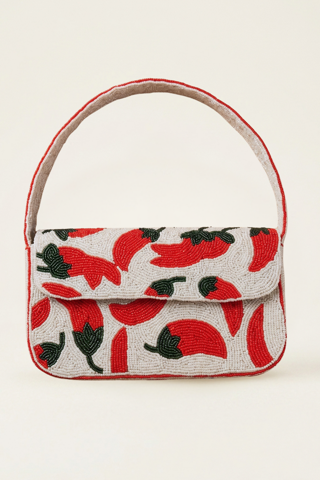 A small structured handbag with a flap front, top handle, and an allover chili pepper print in red and black on a light background, photographed against a plain light beige studio backdrop.