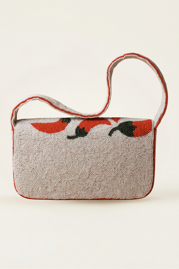 A small rectangular shoulder bag with a textured beige woven body, red trim, and a red and black floral pattern across the top, shown against a plain cream background.
