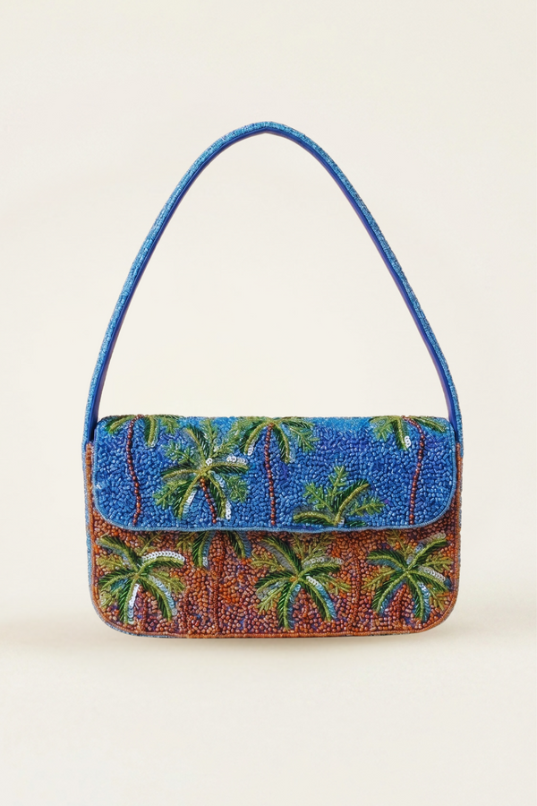 A small rectangular handbag with a blue beaded palm tree pattern and a matching blue shoulder strap, photographed against a plain light beige background.