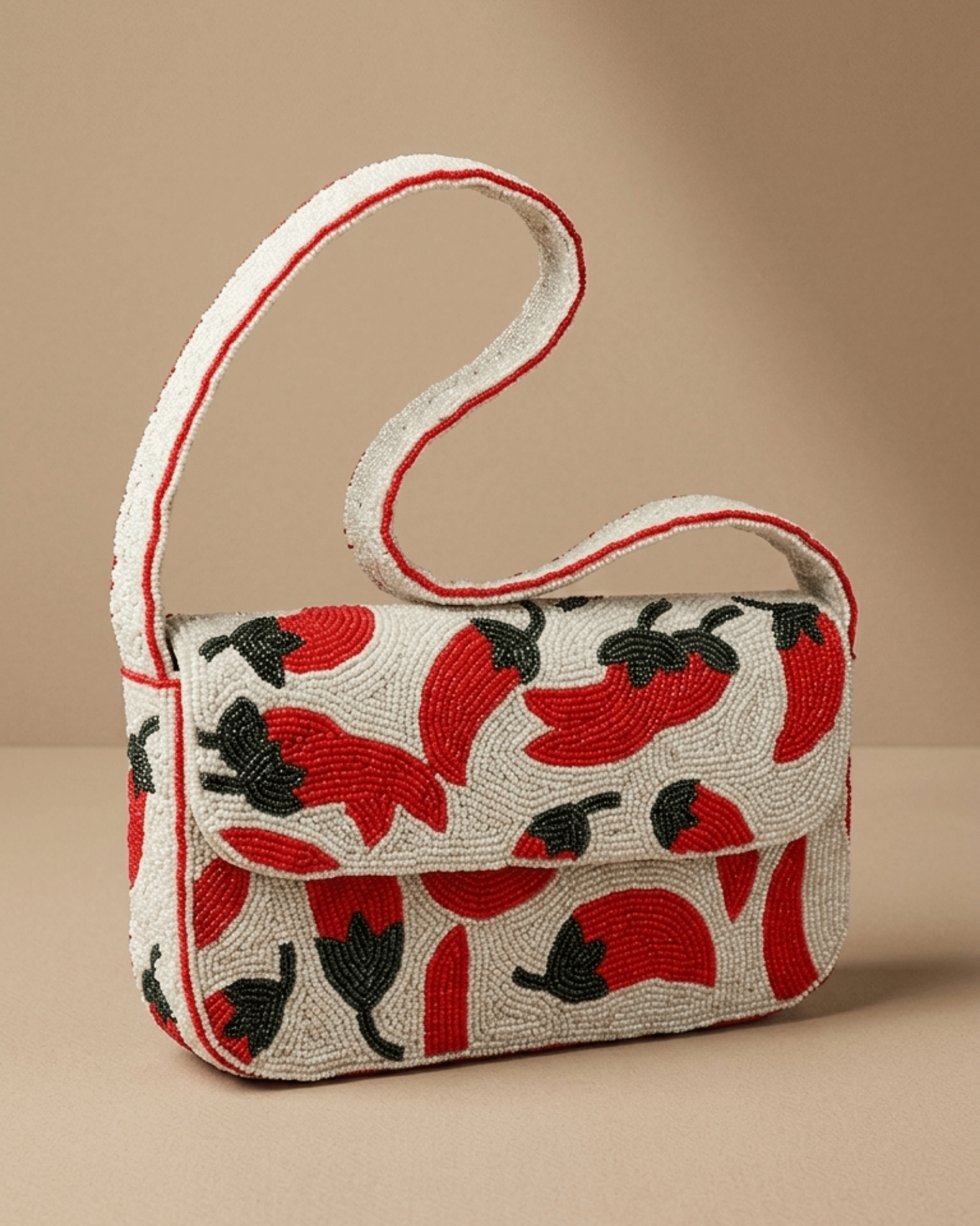 Three-quarter view of The Cayenne hand-beaded chili-pepper shoulder bag with its slim strap looped behind it.