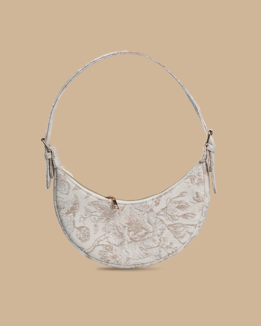 The Flora block-print shoulder bag — three-quarter view of the ivory floral crescent silhouette