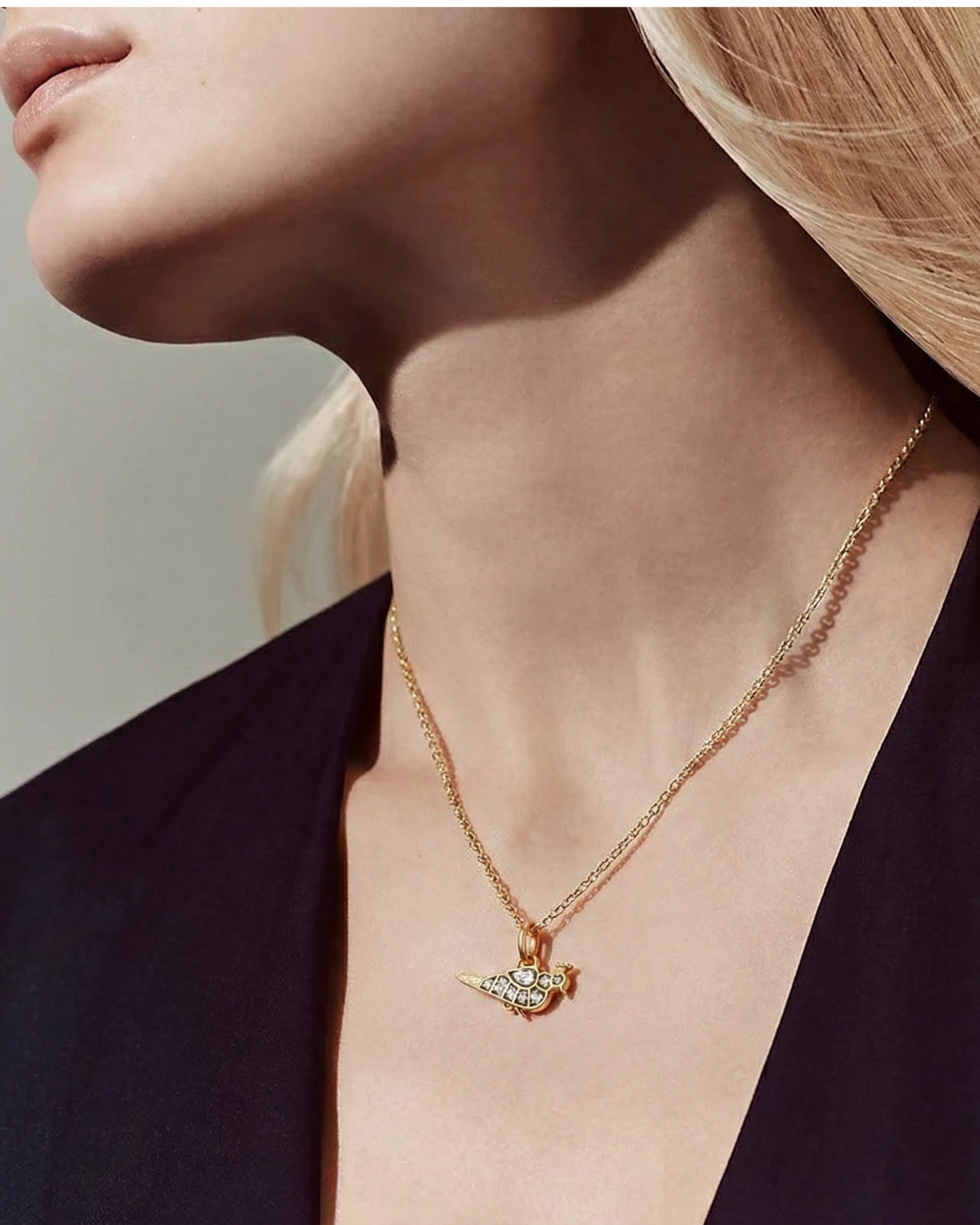 Model wears The Gilded Finch Pendant, a petite gold bird charm with crystal accents, on a fine chain.