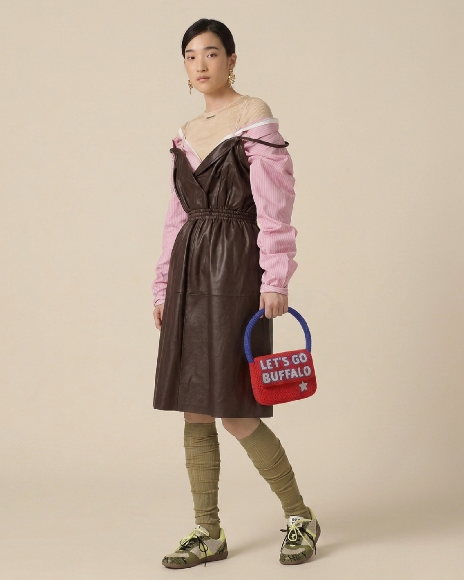 The Rally Buffalo Edition — model in a brown leather dress holds the red beaded ‘Let’s Go Buffalo’ handbag with a blue top handle.