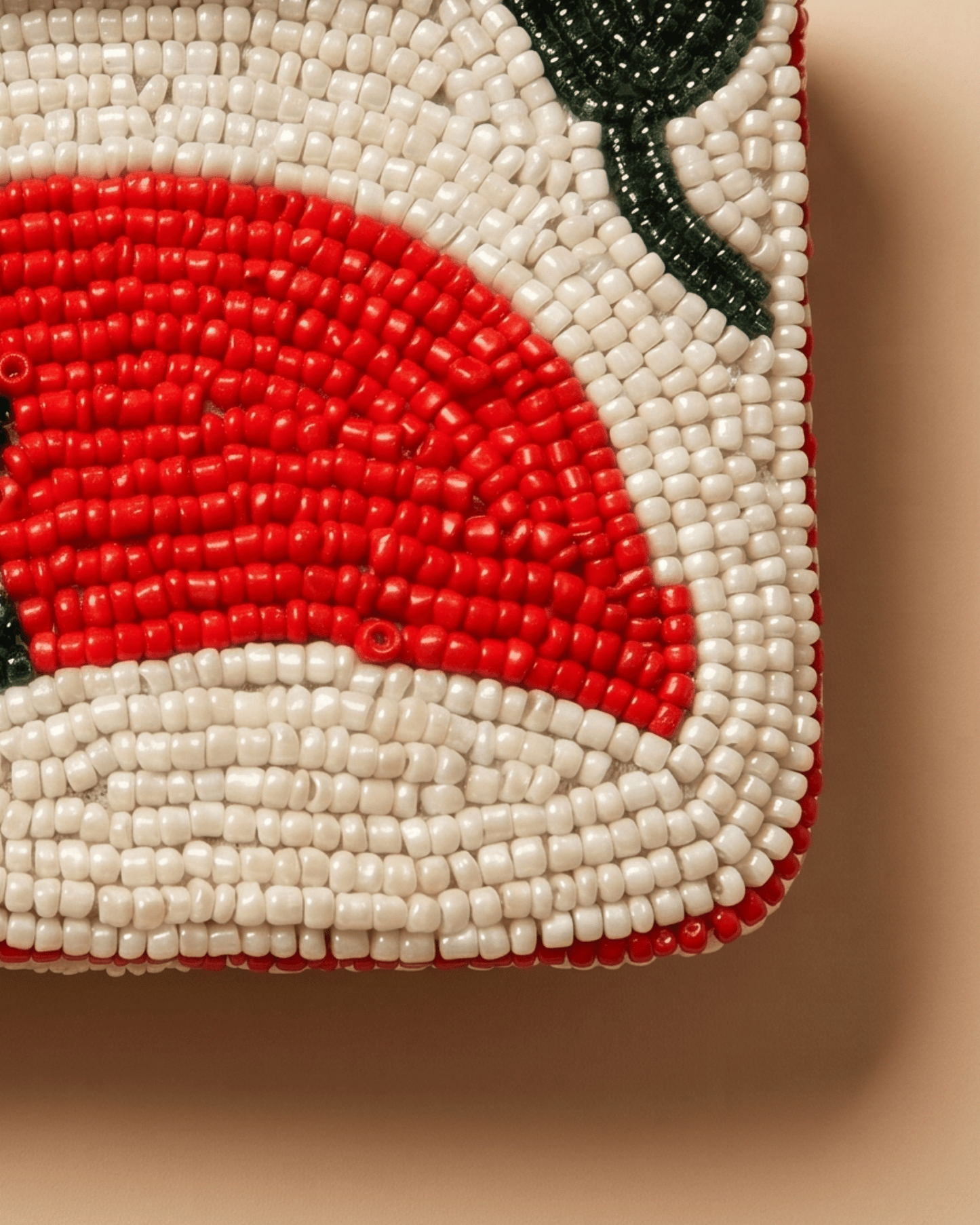 Close-up of The Cayenne's beadwork — a glossy red chili and green leaf set against rows of cream seed beads.