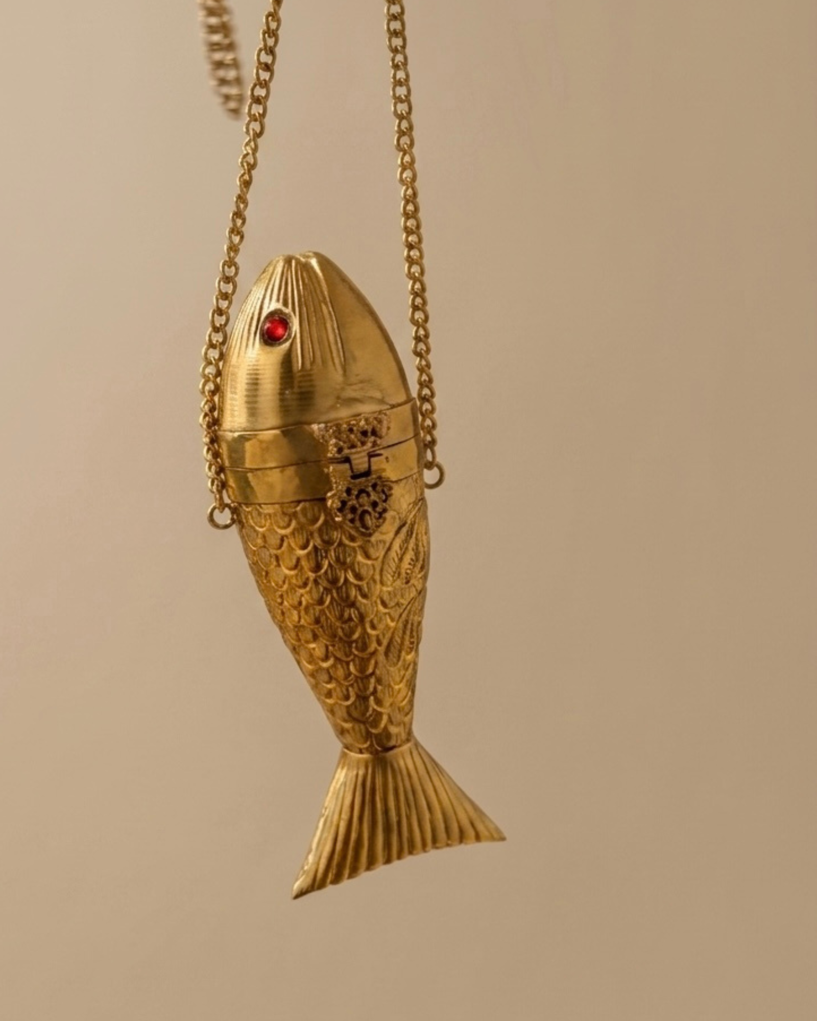 The Siren brass fish minaudière hanging from its chain, detailing the engraved scales, jeweled eye and finned tail.