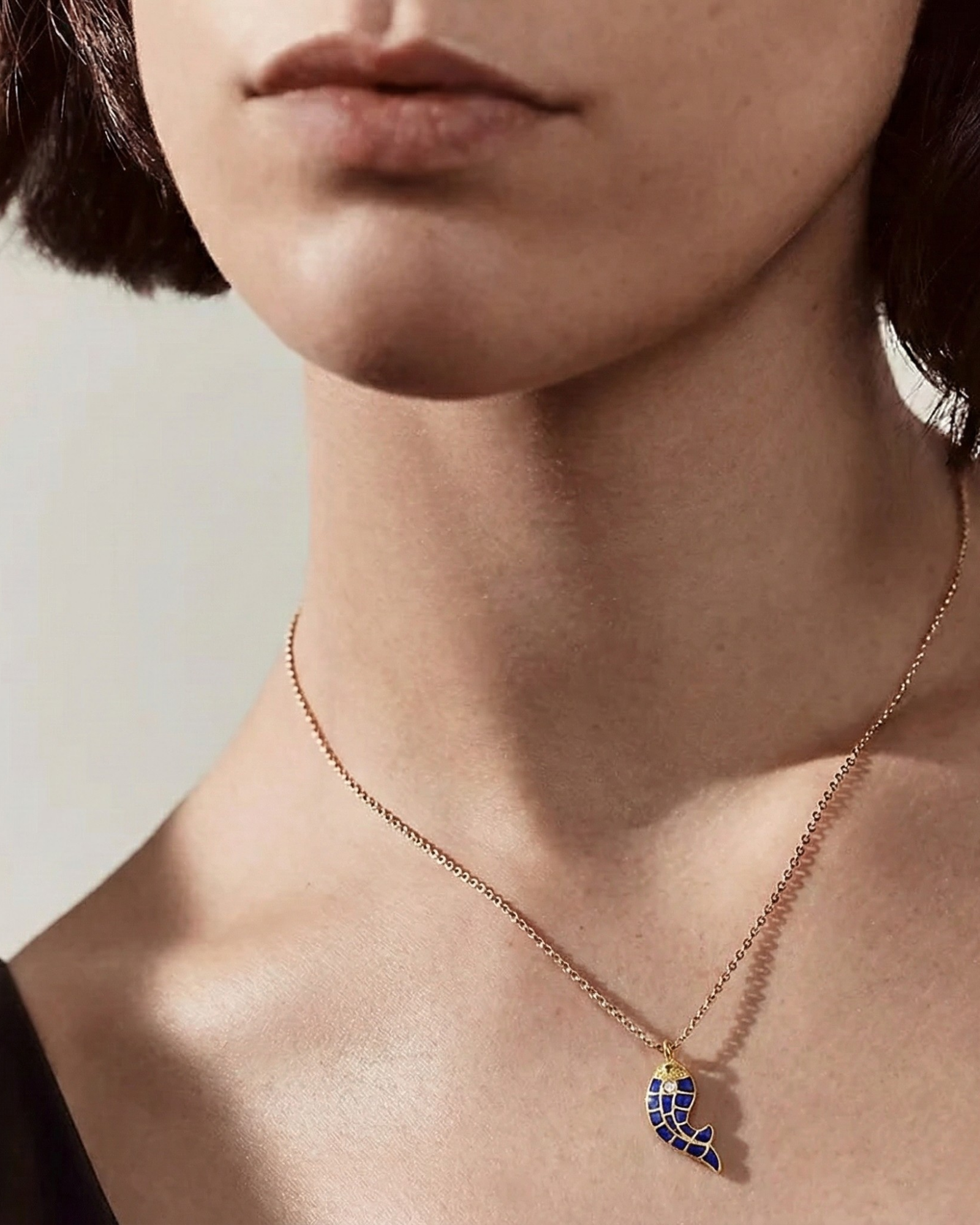 Model wears The Royal Indigo Koi Pendant, a gold koi fish with deep-blue enamel scales, on a fine chain.