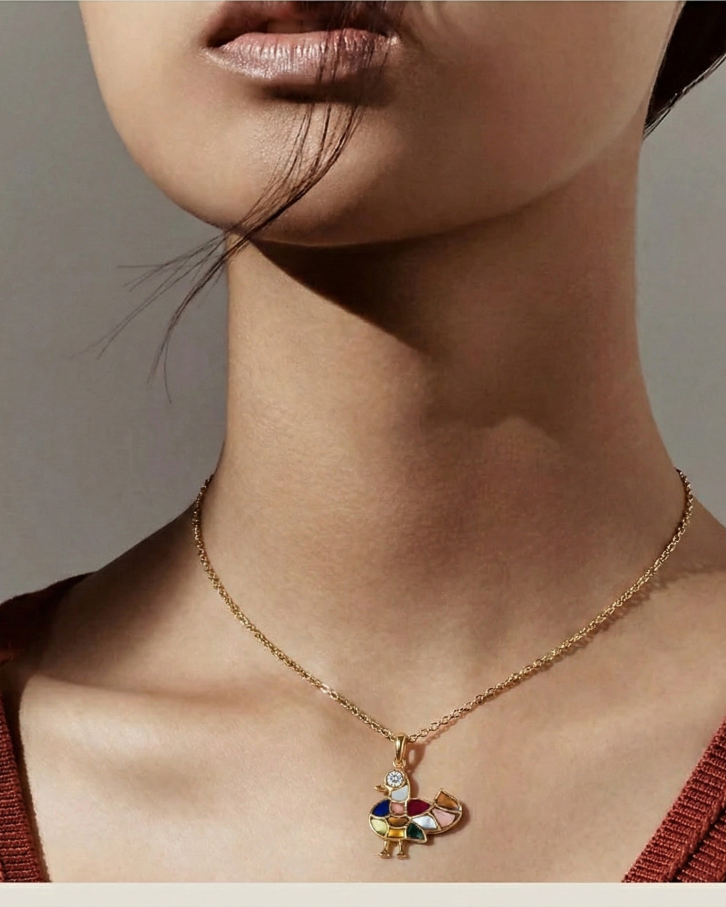 Model wears The Mosaic Mandarin Pendant, a gold bird inlaid with multicolor mosaic stones, on a fine chain.