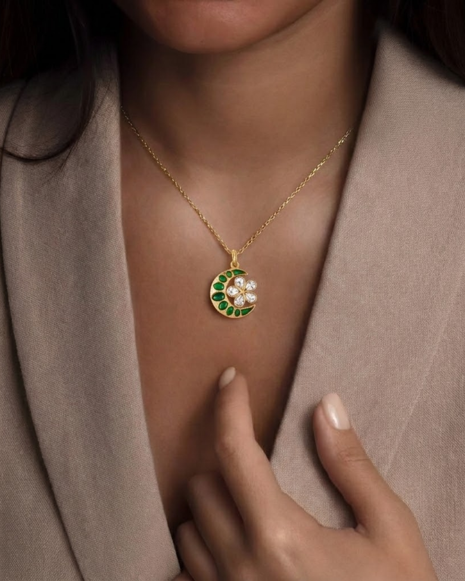 Model wears The Midnight Bloom Pendant, a gold crescent-and-flower pendant set with emerald-green and crystal stones, on a fine chain.