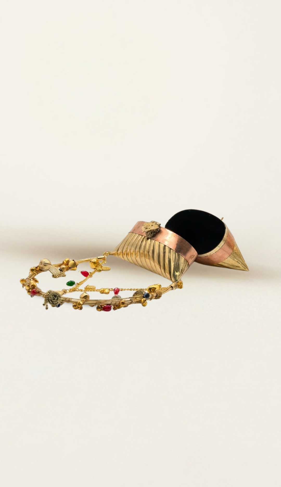 The Nomad two-tone brass bag lying on its side with the lid open, charm-strung handle resting flat