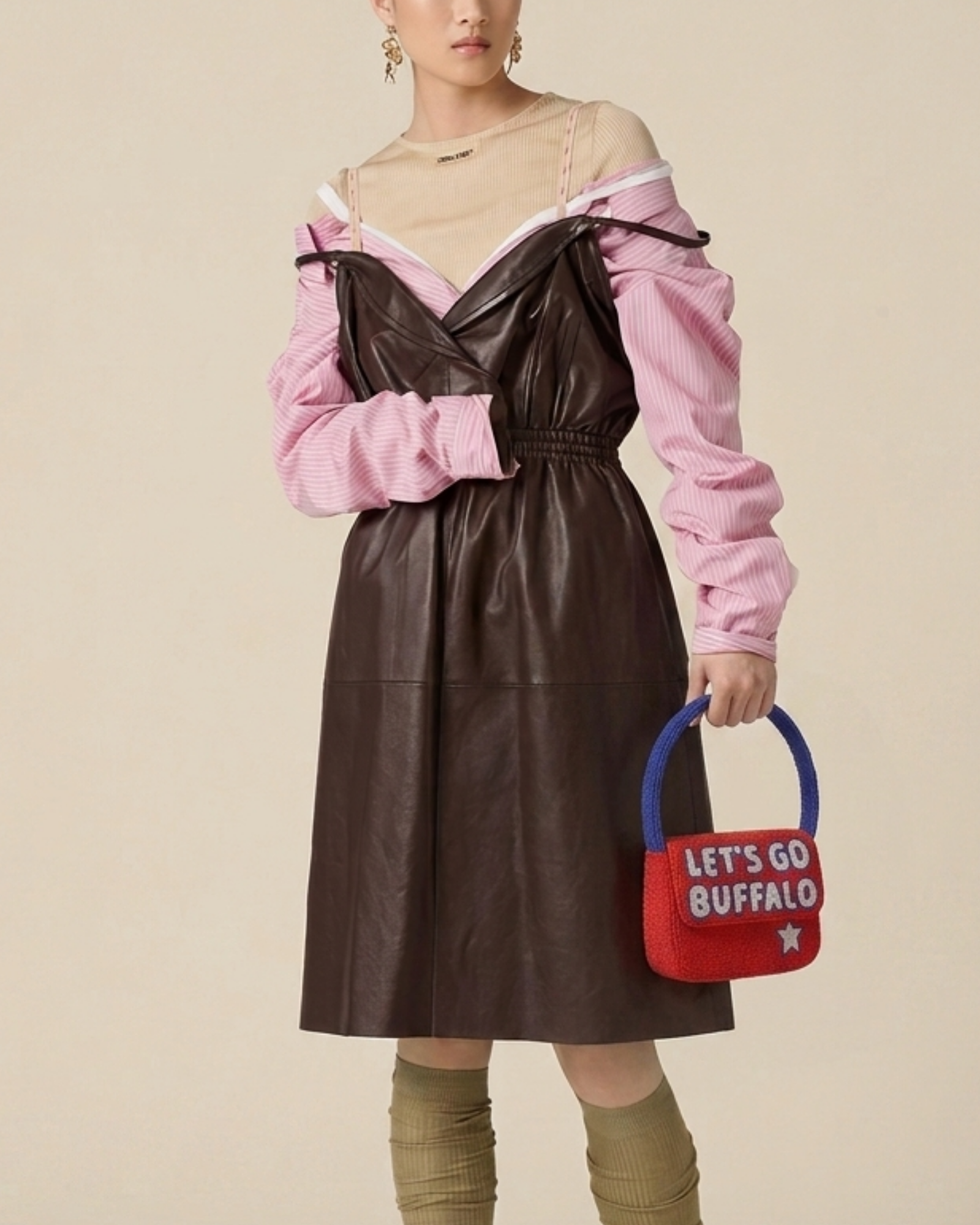 The Rally Buffalo Edition — model in a brown dress and pink top carries the red-and-blue beaded ‘Let’s Go Buffalo’ game-day handbag.