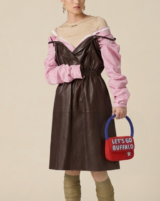 The Rally Buffalo Edition — model in a brown dress and pink top carries the red-and-blue beaded ‘Let’s Go Buffalo’ game-day handbag.
