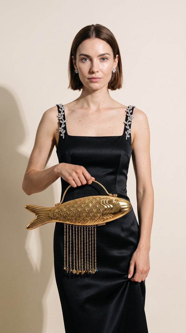 The Monsoon Fish brass clutch carried by its top handle with a black evening gown